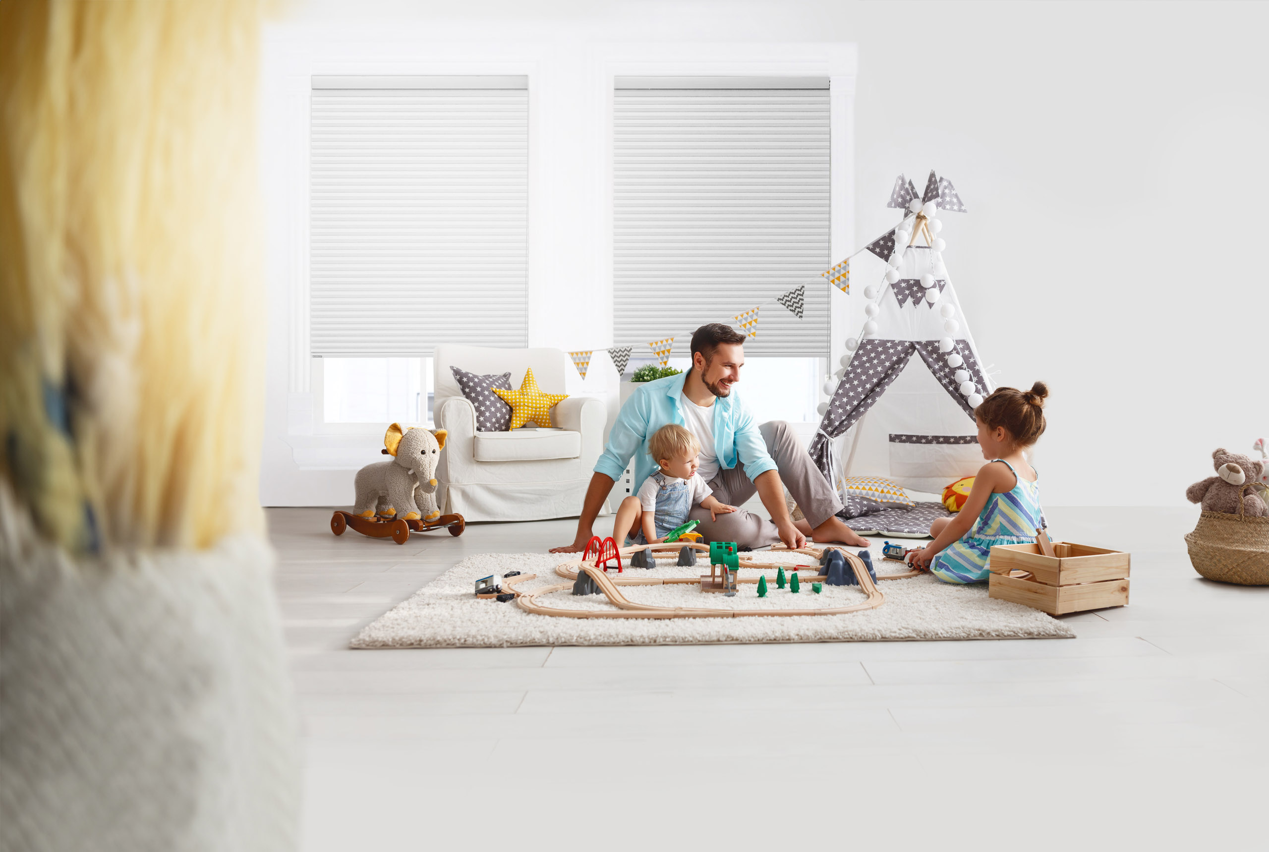 Happy Dad and children playing with a train set enjoying the warmth and comfort from honeycomb blinds